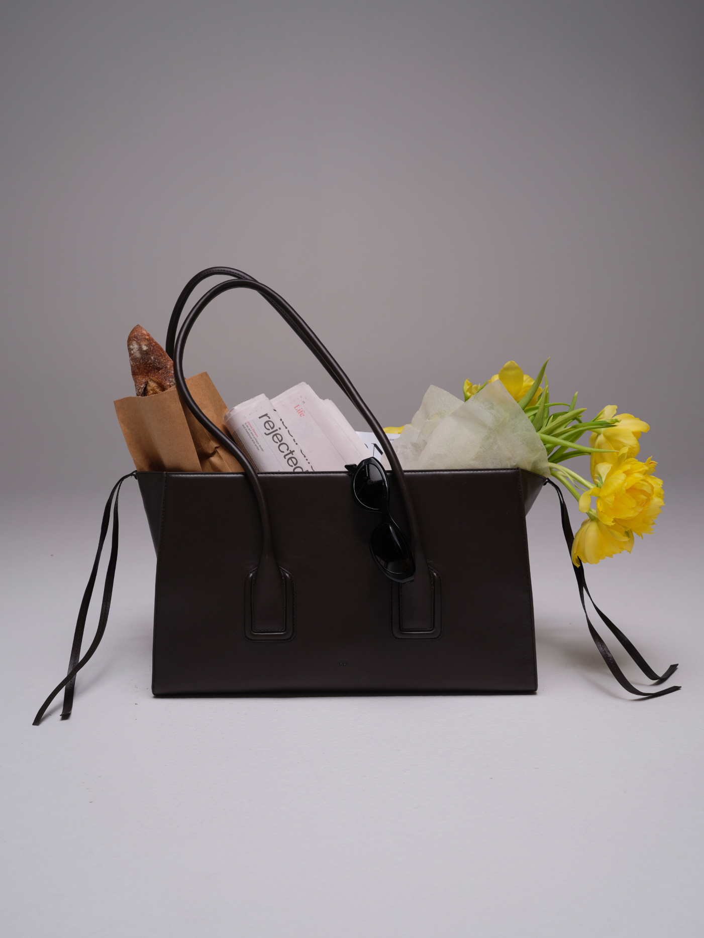 Mateo leather tote in Chocolate holding yellow flowers and everyday items
