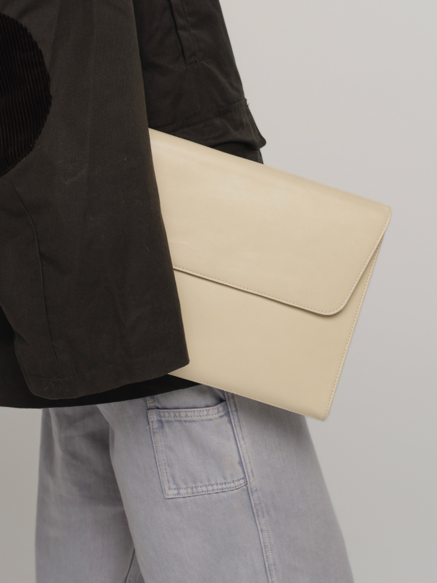Model holding a butter-coloured leather Cleo laptop sleeve against a dark jacket