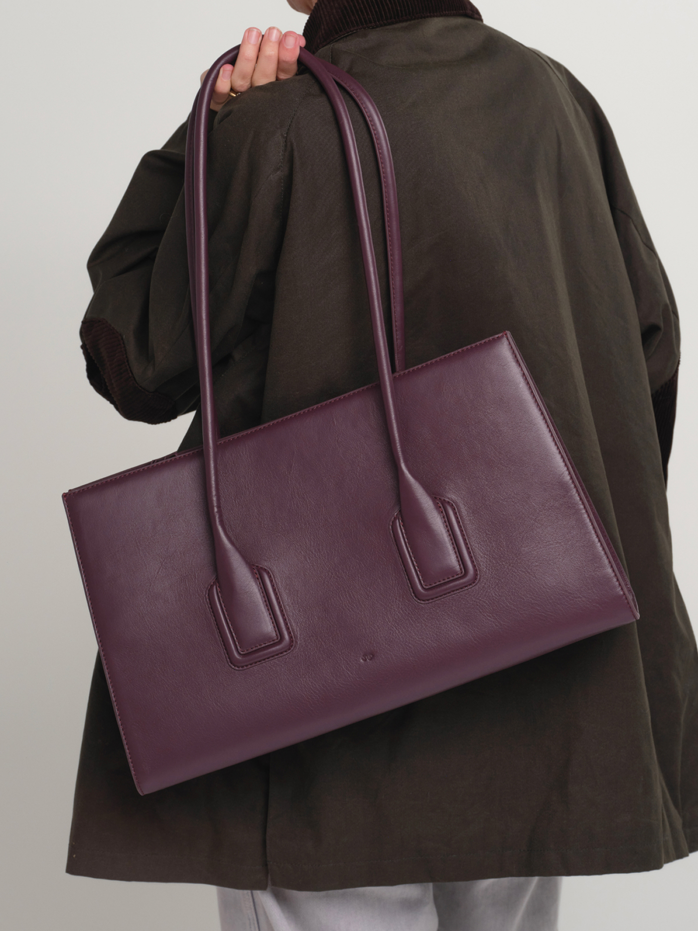 Model in an olive jacket carrying the Mateo leather tote in Fig over her arm